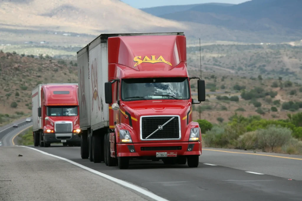 Red freight trucks driving on highway through desert landscape