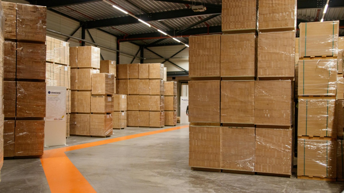 Inside a large warehouse with high stacks of shrink-wrapped wooden pallets
