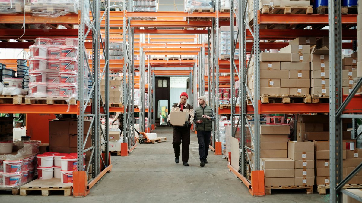Two warehouse workers handling a package surrounded by shelves stocked with boxes, illustrating organized inventory placement.